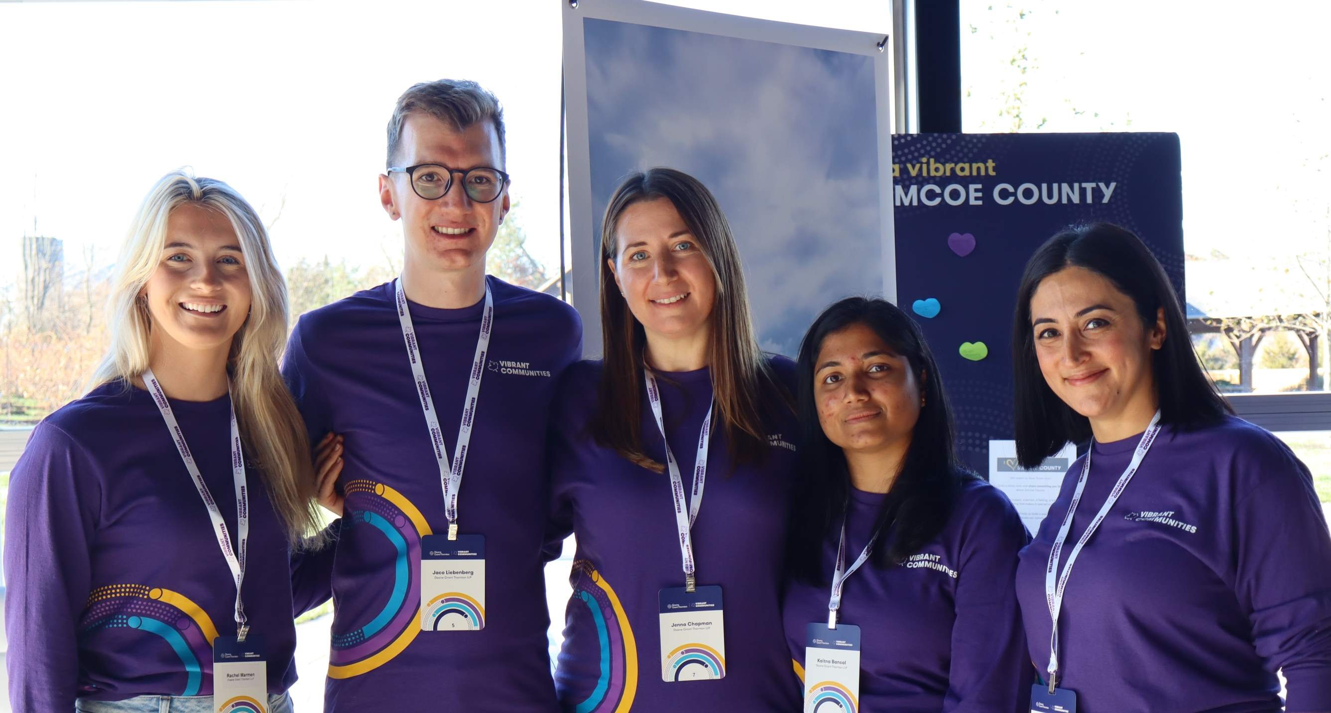 A group of smiling people wearing purple shirts with Vibrant Communities on them stand together