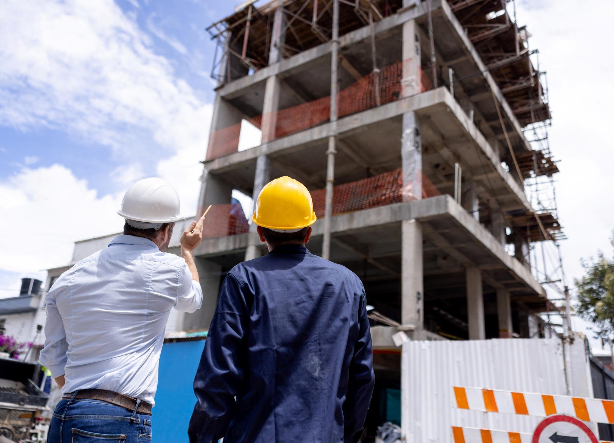 Rear view of an architect talking to the building contractor at a construction site and looking at the frame