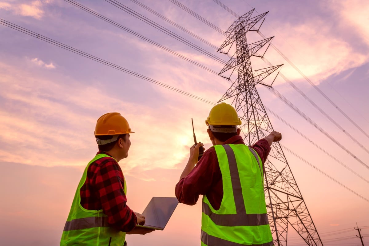 Two people in high visibility vests survey power line infrastructure