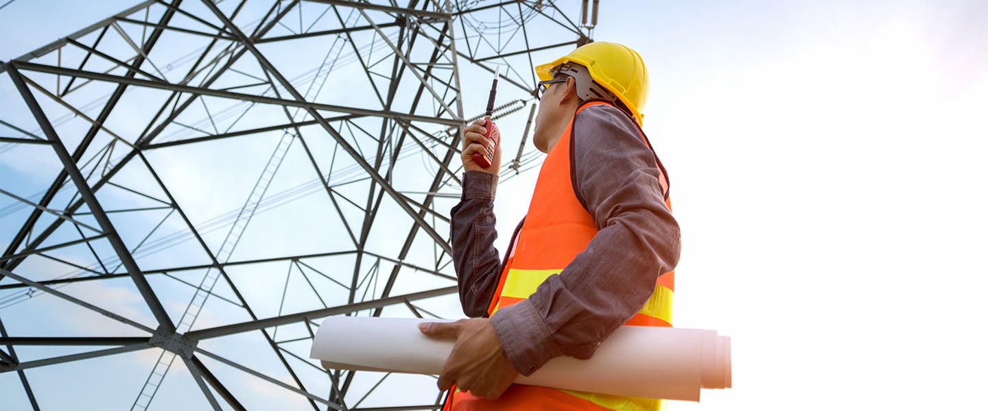 A man on a walkie talkie inspects a transmission tower